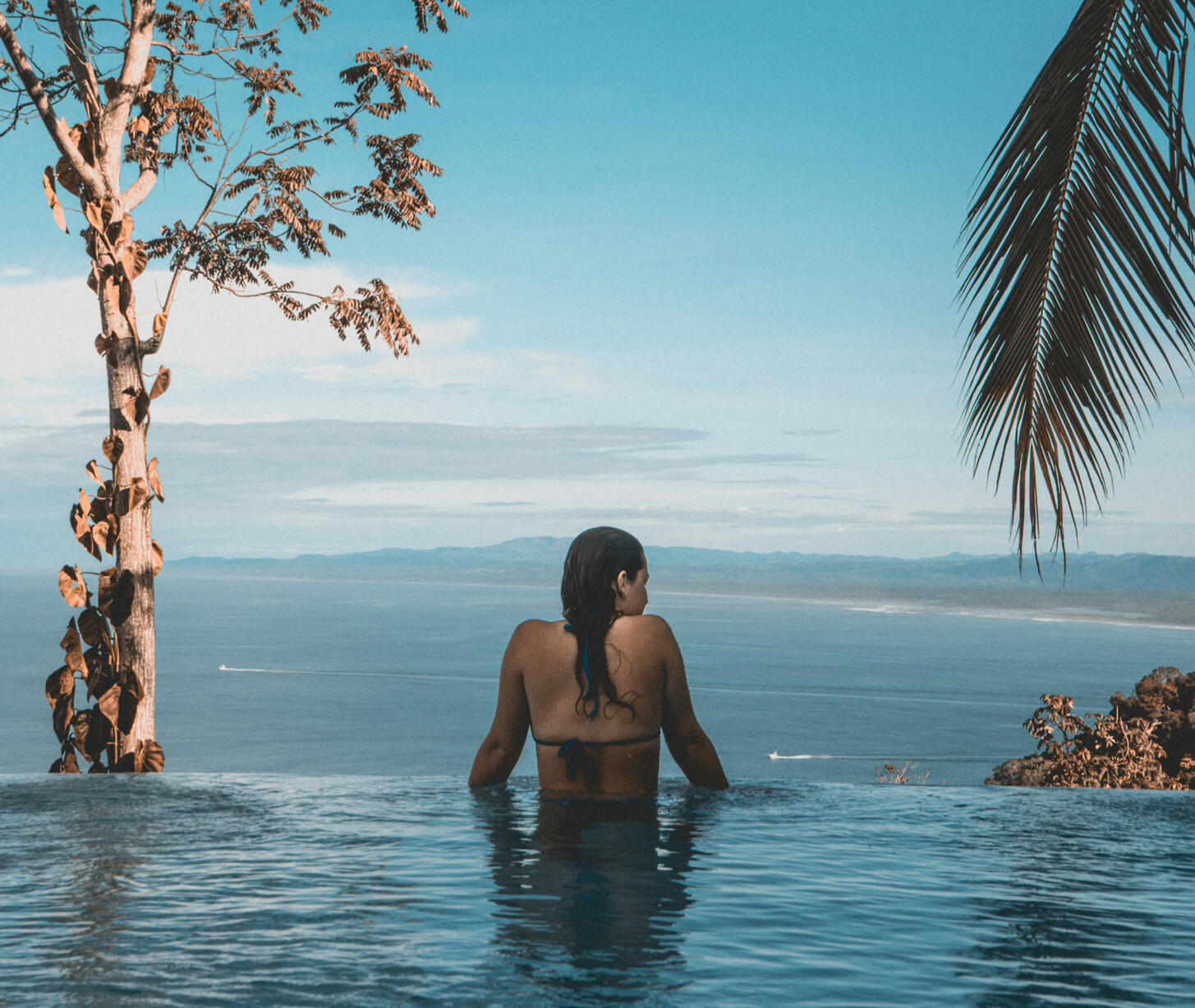 Soaking in the view Luxury traveler in an infinity pool in a tropical location gazing at the ocean.